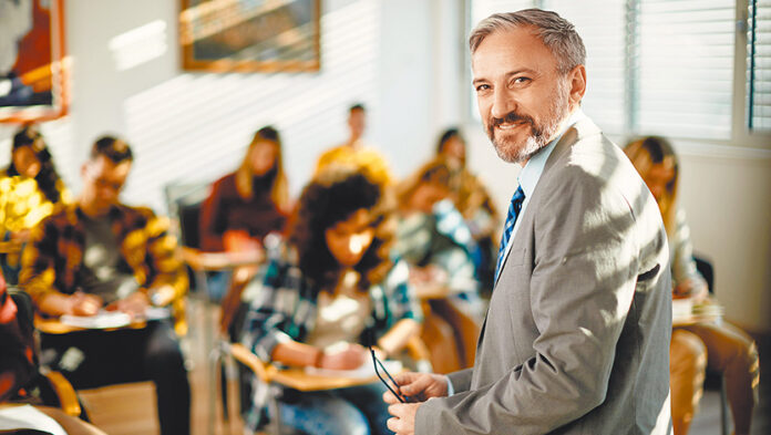 Happy mature teacher in the classroom looking at camera.